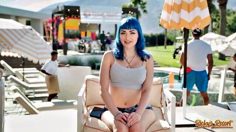 Blue-haired skinny babe with medium tits sits poolside in tank top and shorts at Cayla's Resort