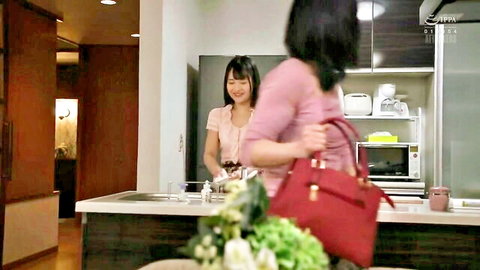 Two smiling Japanese women in pink tops chatting in modern kitchen holding red handbag