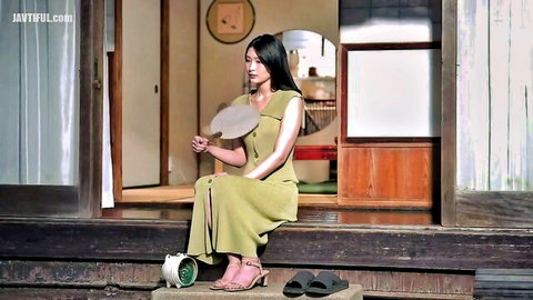 Sexy Japanese beauty in tight green slit dress sits teasing with fan and long legs