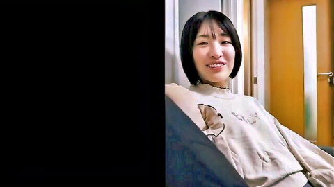 Cute Asian college girl smiling seductively in cozy sweater on couch