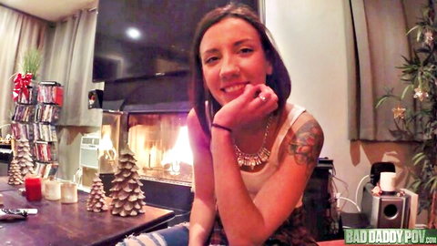 Smiling brunette with tattoos and small tits in low-cut tank top by Christmas fireplace POV