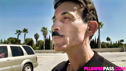 Mature man with thick mustache poses outdoors by SUV in sunny parking lot