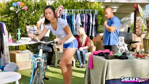 Skinny brunette teen babe in tight shorts bends over bike on outdoor patio