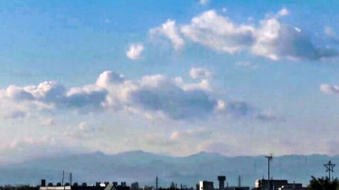 Scenic blue sky with fluffy white clouds over distant mountains and urban skyline