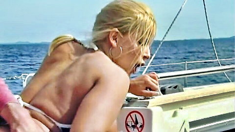 Blonde in pink bikini leaning forward on yacht, erotic outdoor scene