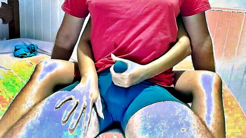 Woman's hand holds blue ball teasingly over man's crotch in blue shorts on bed