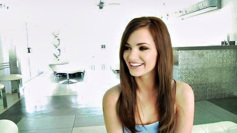 Smiling young brunette with small tits and long hair posing in tight tank top on couch