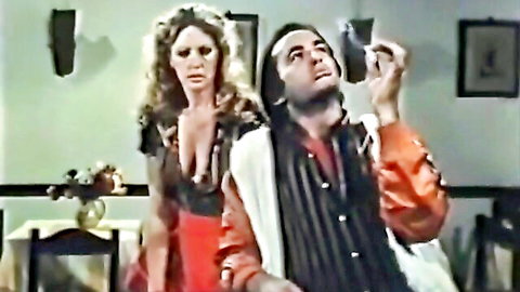 Vintage 1980s erotic film scene with busty curly-haired woman in low-cut dress and man holding prop