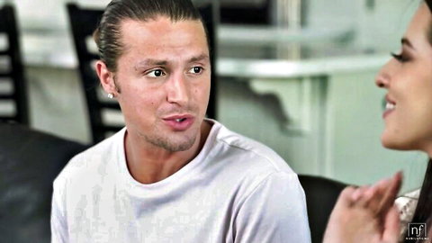 Ponytail guy in white tee gazes at smiling sexy brunette babe on couch in hot episode