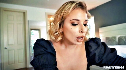 Ivy LeBelle teases with tongue out, blonde bob in low-cut black top, seductive close-up