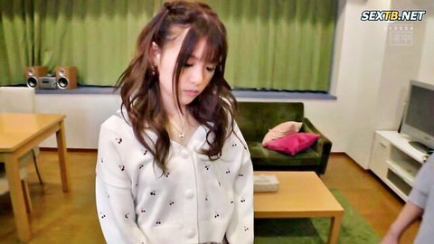 Shy Japanese teen with long hair looks down wearing white cardigan in living room