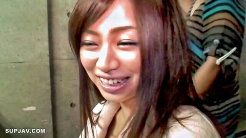 Young skinny Japanese brunette with long hair smiles teasingly with friend in tight tops