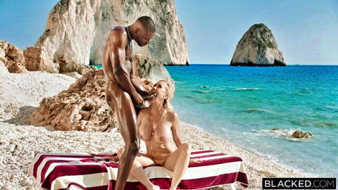 Tanned blonde with big tits kneels nude on beach gripping muscular black man's huge erect BBC as he pulls her long hair