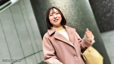 Smiling Asian woman in pink coat and cream turtleneck posing outdoors with bag