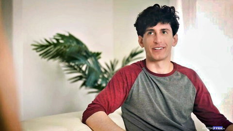 Curly-haired man smiling on white couch in gray red raglan shirt lounge
