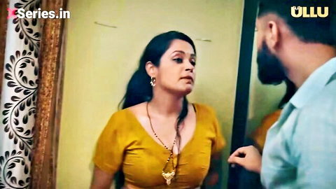 Indian MILF housewife with big tits in tight yellow blouse stands before mirror as bearded man eyes her cleavage hungrily