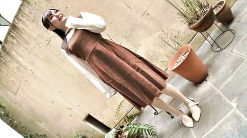 Cute Japanese brunette smiling playfully in short brown dress teasing legs outdoors