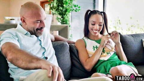 Bald DILF stepdad smiles at hot teen cheerleader in green uniform skirt on couch