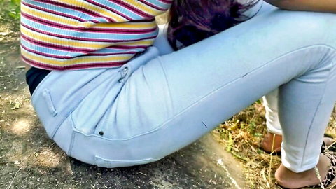 Priya squatting in tight blue pants outdoors, showing curvy ass