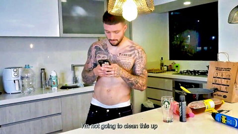Tattooed muscular hunk Rauls Bud in underwear, checking phone in messy kitchen after sex