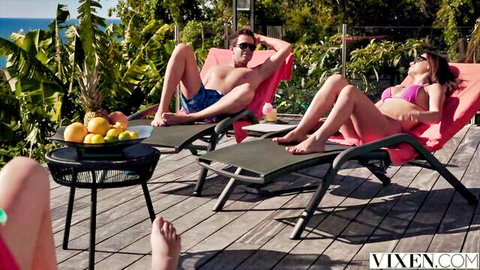 Sexy bikini babe lounging poolside with handsome guy in trunks on sunny deck