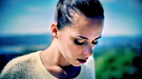 Eva in scenic outdoor portrait, brunette with bun, wearing cozy sweater, gazing down