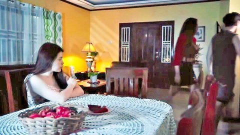 Amateur Asian babe in tank top sitting at table eating grapes in home kitchen