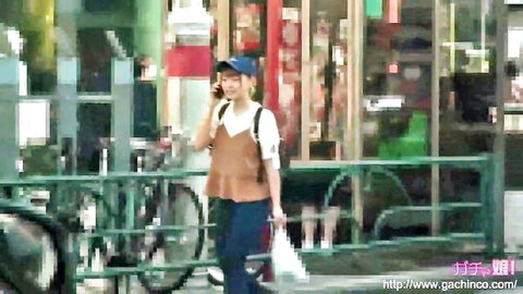Asian woman in casual tank top, vest, jeans and cap walking street talking on phone