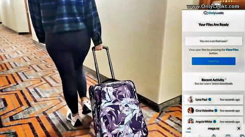 Hotwife Lauren in plaid shirt and tight pants, walking hallway with suitcase