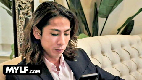 Asian man in suit on couch holding phone, Mylf thumbnail for pale juicy BBW with nipple piercings
