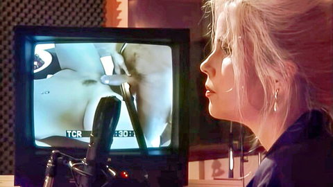 Blonde woman intently watches CRT TV showing close-up of big tits babe's exposed pussy with microphone inserted