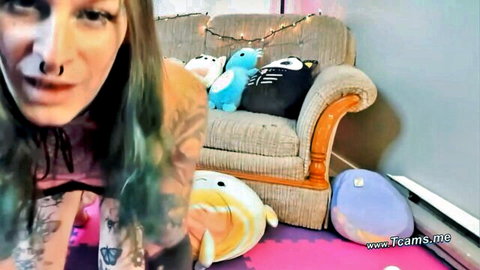 Tattooed woman with dyed hair lounging with plush toys in intimate setting
