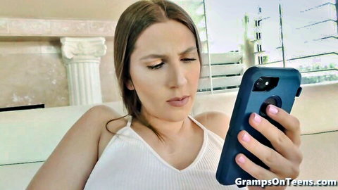 Skinny young brunette with small tits in white tank top looking at phone