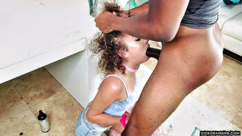 Petite curly-haired girl in pink collar giving blowjob to black man