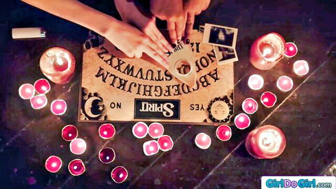 Women's hands on Ouija board with planchette amid pink candles and incense in dark ritual