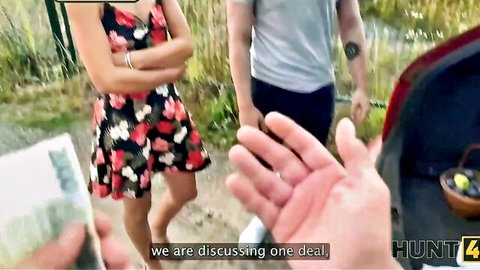 Sexy babe in short floral dress discusses hot deal with strangers outdoors by car trunk