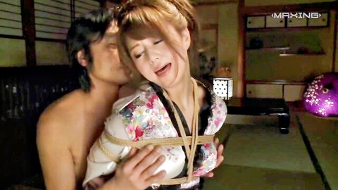 Japanese woman bound in shibari ropes with exposed tits embraced and kissed by shirtless man