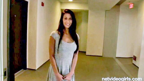 Young brunette amateur smiles in tight gray dress showing cleavage in hotel hallway casting