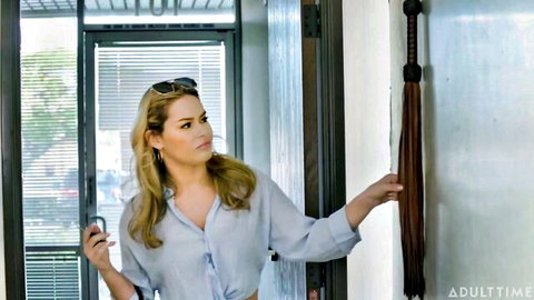Katrina Colt in loose blue shirt holding phone in AdultTime scene