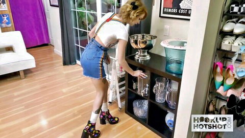 Blonde babe in short fringed denim skirt and suspenders bends over browsing high heel shelves teasing