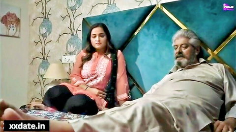 Young desi girl in pink salwar kameez sits on bed beside older bearded man lying down