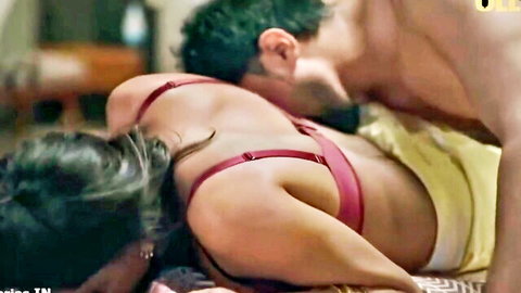 Brunette woman in red bra passionately kissed on neck by muscular shirtless hunk on bed