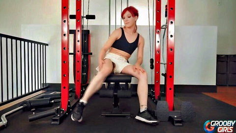 Redhead trans babe in sports bra and shorts spreads legs wide on gym bench teasing bulge
