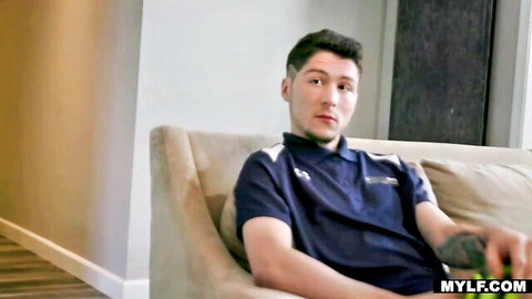Handsome young stepson lounging on couch playing video games in tight polo shirt