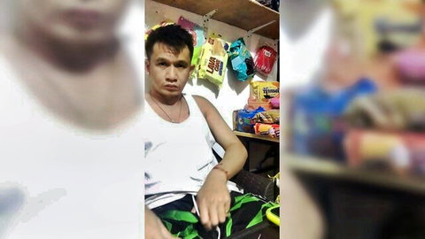 Asian man in white tank top and green shorts sitting in snack store