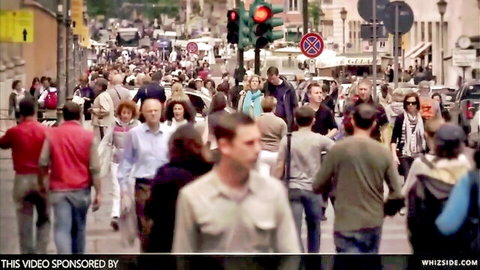 Busy urban street scene with crowd crossing at red traffic light
