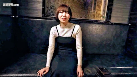 Cute Asian girl in white turtleneck and black slip dress smiling on black leather couch