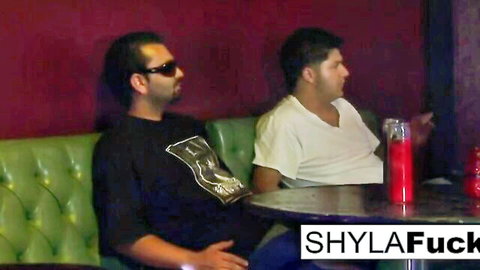 Two bearded men lounging on green couch in red club with drinks and candles