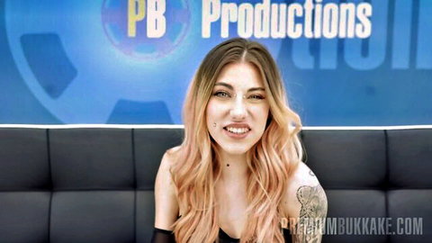 Skinny young fair-skinned woman with long wavy pink hair smiles in clothed bukkake interview
