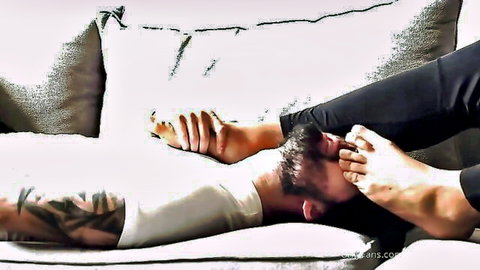 Tattooed gay hunk lies on couch grabbing and sucking smooth male toes in foot worship